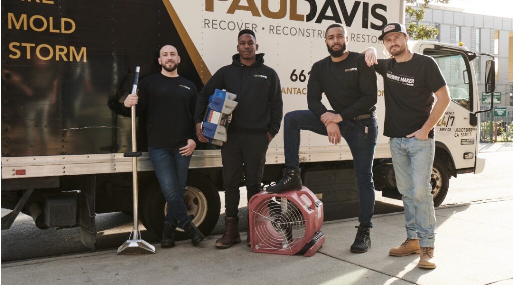 Paul Davis Restoration of Asheville team members standing in front of a service truck with restoration equipment, including a floor fan and tools, ready for water, fire, and mold damage response.